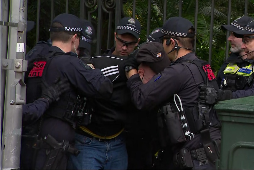 A person dressed in dark clothes being detained by several police officers.