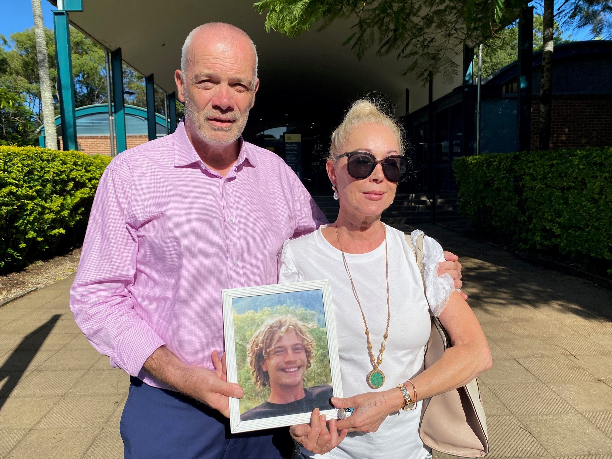 Parents Sandra MacFarlane and Ian Stacker standing outside Byron Bay Court holding a photo of their don Jackson.