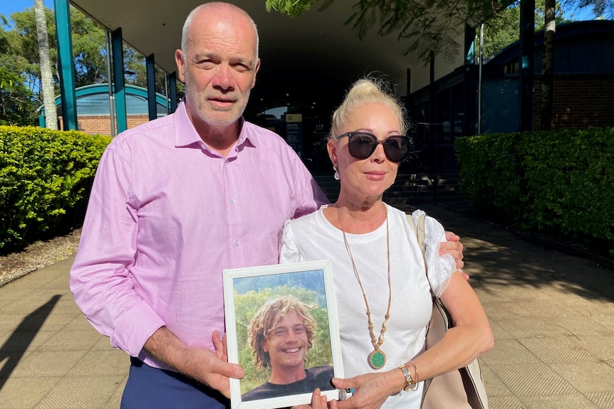 Parents Sandra MacFarlane and Ian Stacker standing outside Byron Bay Court holding a photo of their don Jackson.