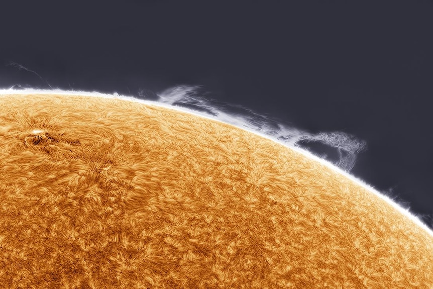 An extreme close up image of the sun with clouds seen around the edge. 