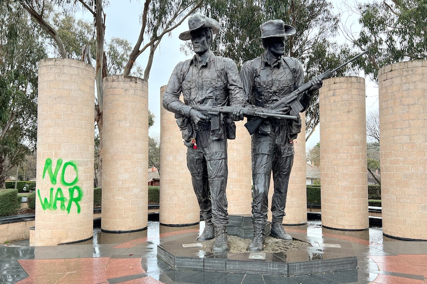 Green writing saying "no war" beside  a war memorial.