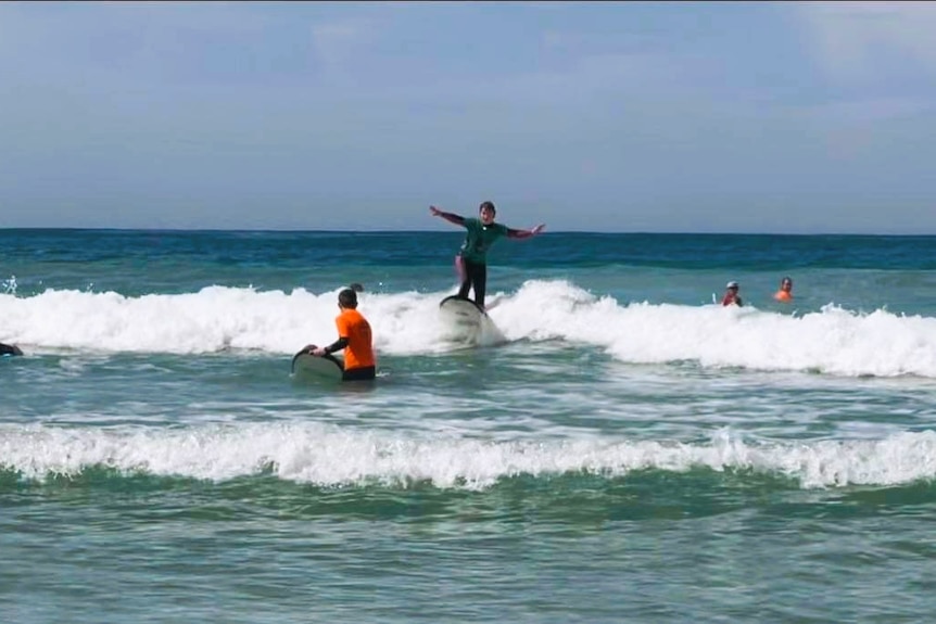 beginner surfer standing up on board in distance on wave