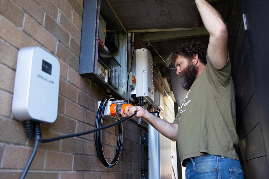 A bearded man plugs in an electric charging cord 