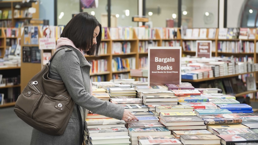 Woman leaning over table of books in bookstore.