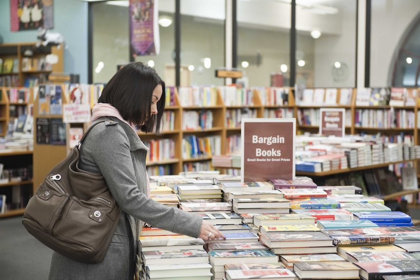 Woman leaning over table of books in bookstore.