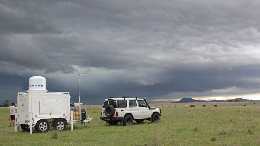 A white weather monitoring trailer in a field with a white landcruiser.