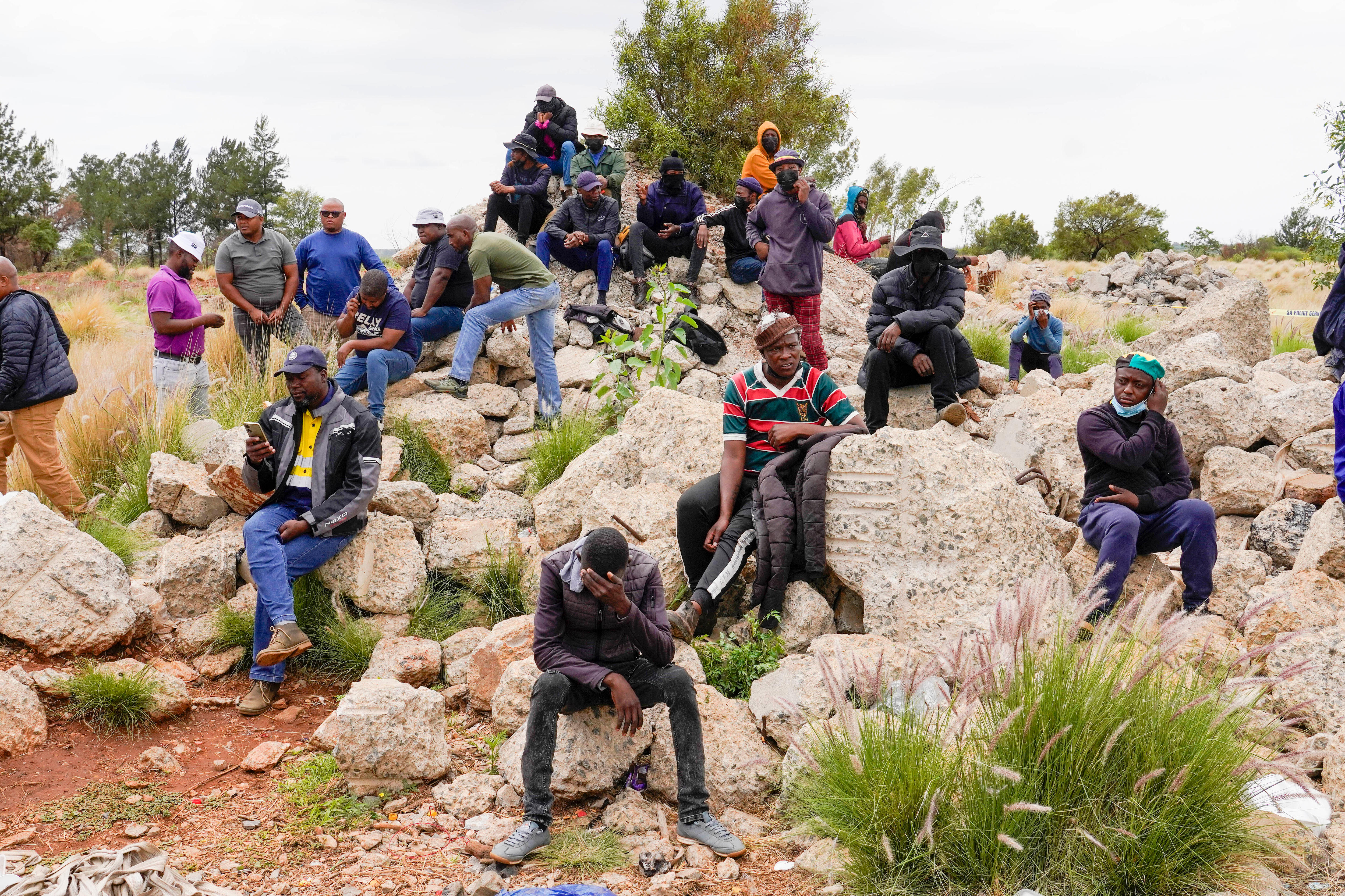 Volunteer rescuers sit on rocks by the opening of a gold mineshaft where illegal miners have been trapped underground.