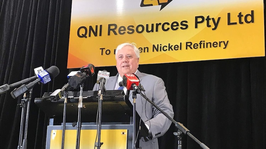 Clive Palmer stands at a podium surrounded by microphones and a sign announcing the reopening of the QNI Resources refinery