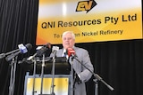 Clive Palmer stands at a podium surrounded by microphones and a sign announcing the reopening of the QNI Resources refinery