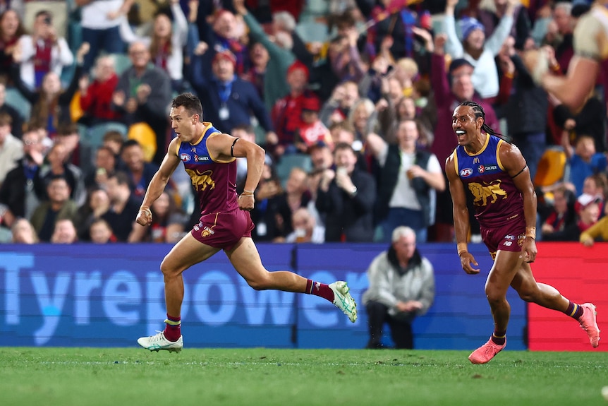 A Brisbane Lions AFL player races across the field with a teammate after scoring a vital goal.