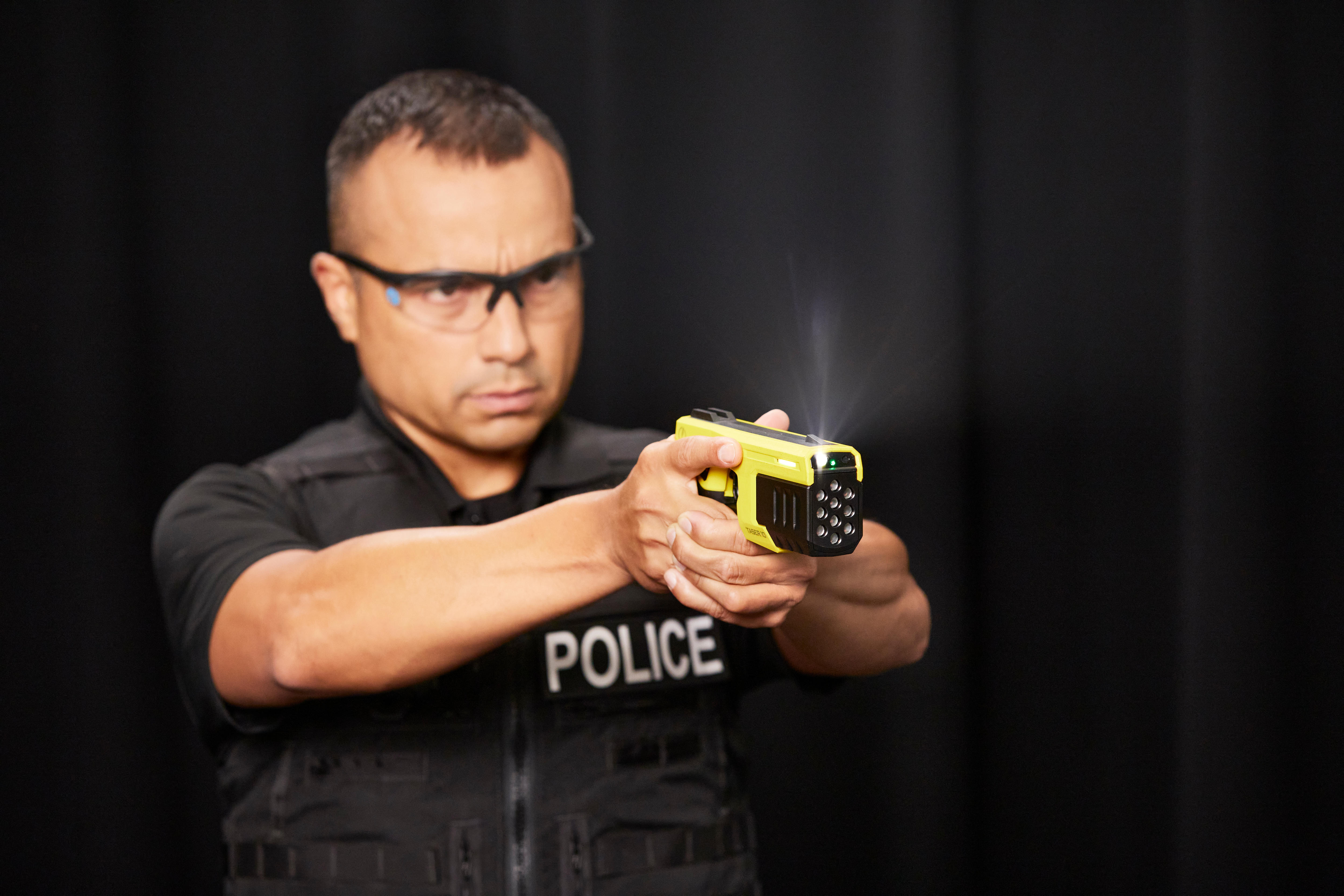 Man in police wearing glasses uniform holds yellow and black Taser 10 in promotional photo, light coming from device