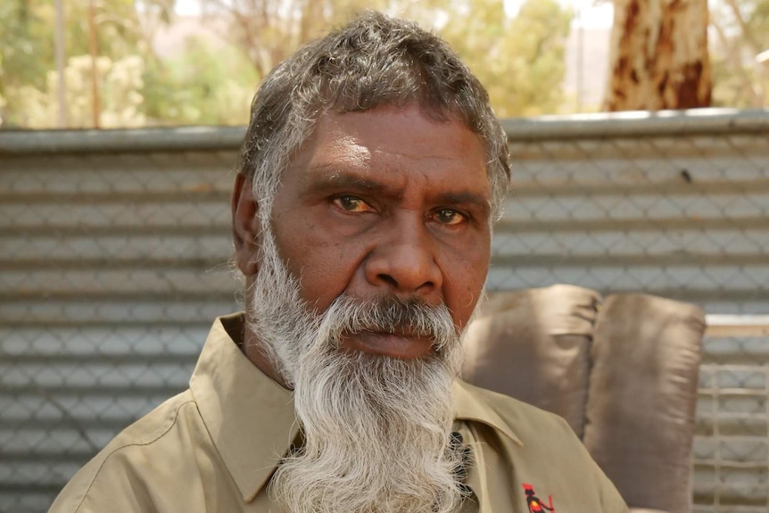 A middle-aged man with a flowing white beard looks at the camera