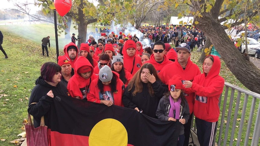 People dressed in red hoodies marching while carrying a large Indigenous flag