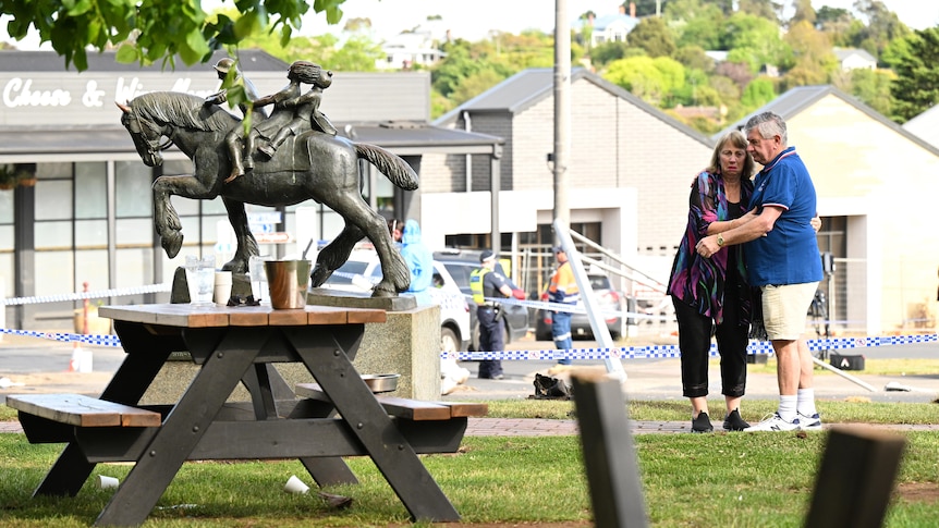 A man and woman hug next to police tape at Daylesford after a fatal crash.