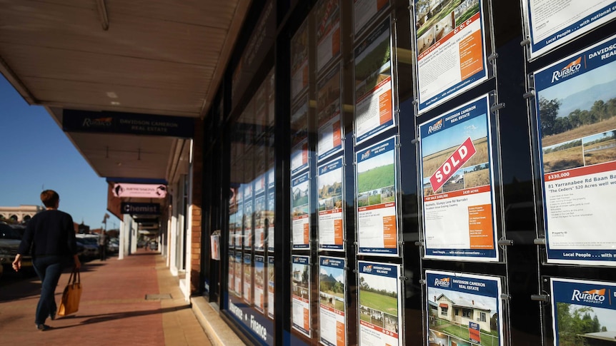 A woman walks past for sale signs in the window of RuralCo real estate agents in Narrabri, NSW.