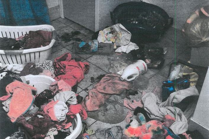 A dirty laundry with clothes and animal faeces on the floor.