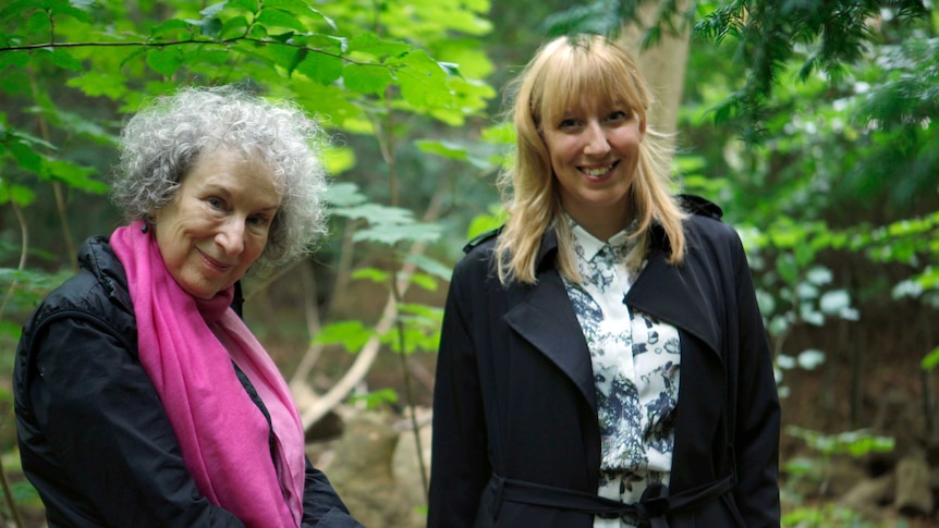 Two women standing in a forest smiling and looking at the camera.