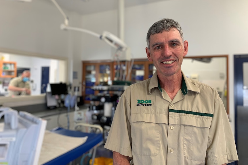 A man in a zookeeper's uniform smiles at the camera. 