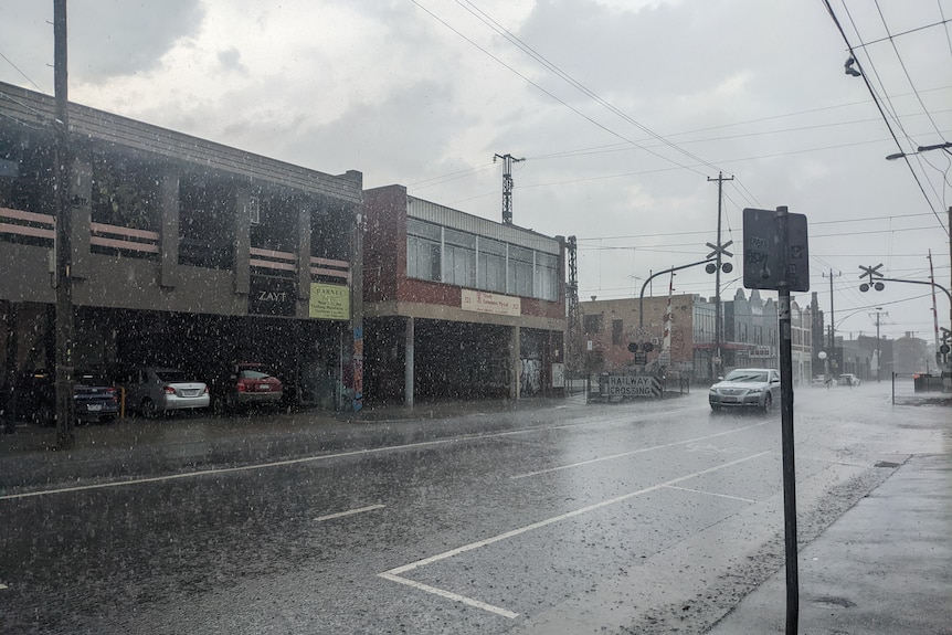 A rainy streetscape. Large droplets are visible and the road is soaked