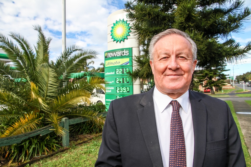 A man stands on a footpath outside a petrol station.