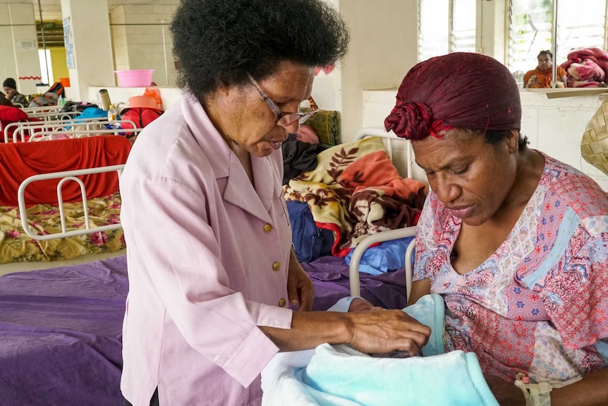 A nurse in a PNG hospital hands a baby to its mother