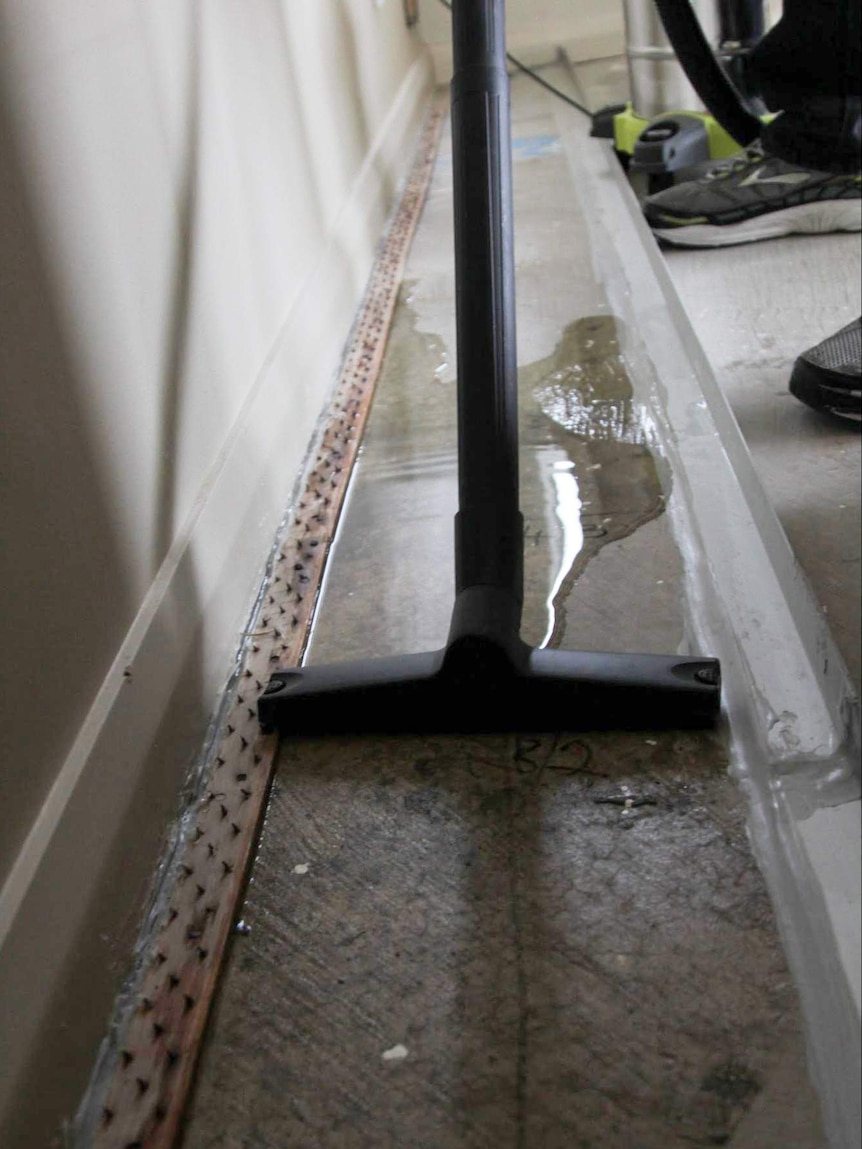 John vacuums water out of the dam in the living room of his apartment in Wentworth Park.