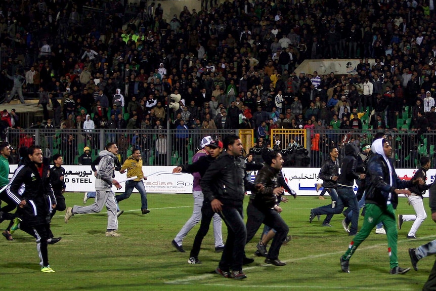 Football fans rush across the pitch during clashes after a match between Al-Ahly and Al-Masry.