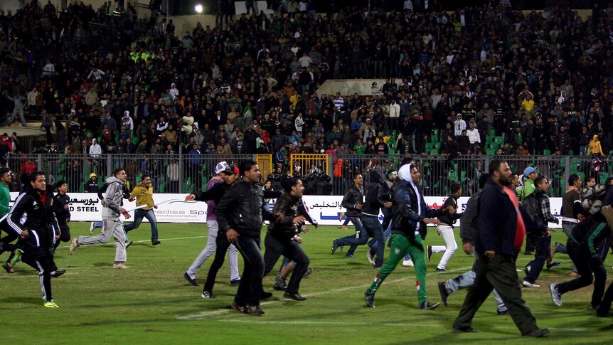 Football fans rush across the pitch during clashes after a match between Al-Ahly and Al-Masry.