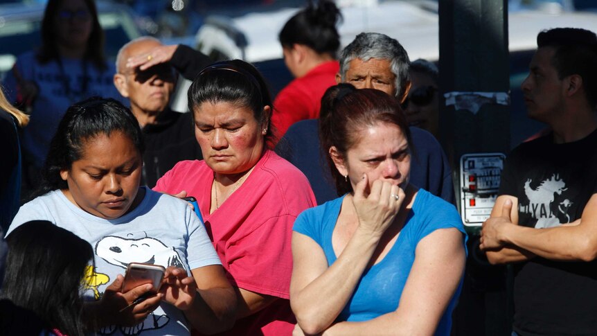 Nervous looking parents chew nails and wait on mobile phones outside a school