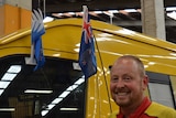 Nik Wilson stands next to his post van with the current NZ flag and its possible replacement flying from the door.