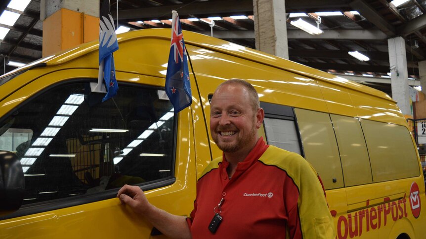 Nik Wilson stands next to his post van with the current NZ flag and its possible replacement flying from the door.