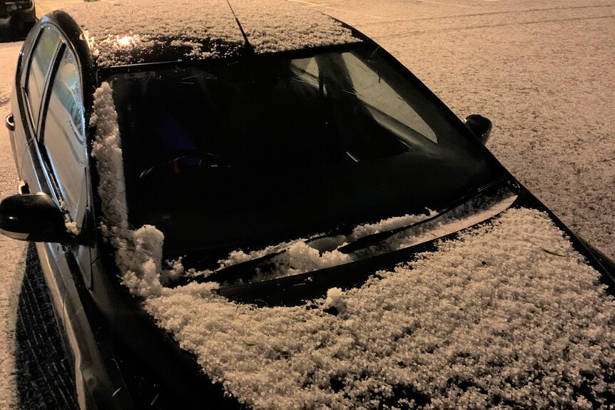 A car covered in hail with the ground around it also white with hail