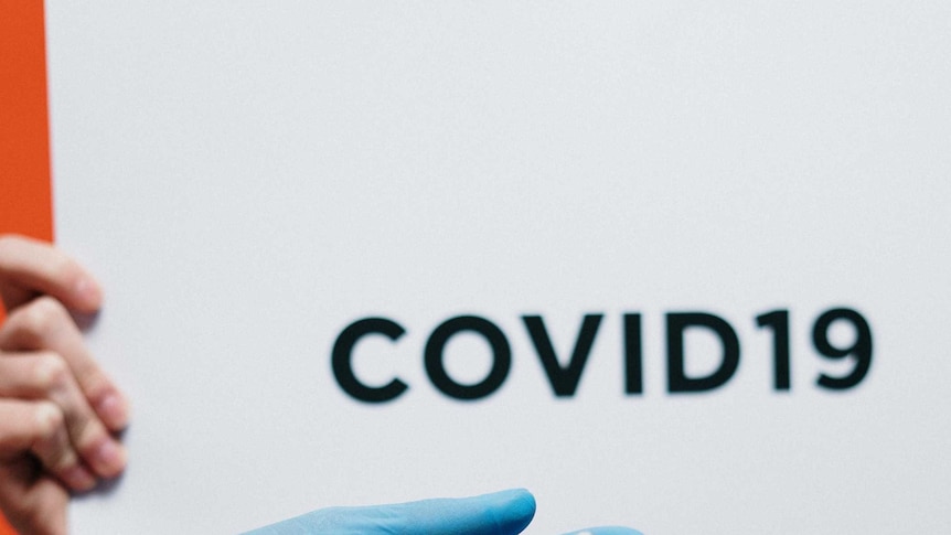 Photo of a sign saying 'COVID' and a gloved hand with a syringe and bottle