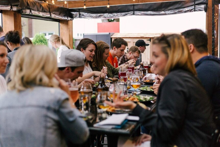 Personas sentadas en una mesa larga compartiendo comida y bebidas.