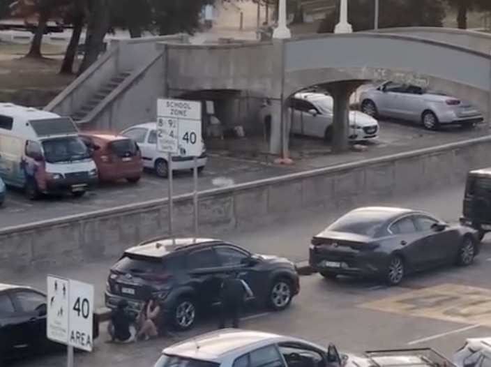Filas de coches aparcados con gente agachada detrás de ellos.