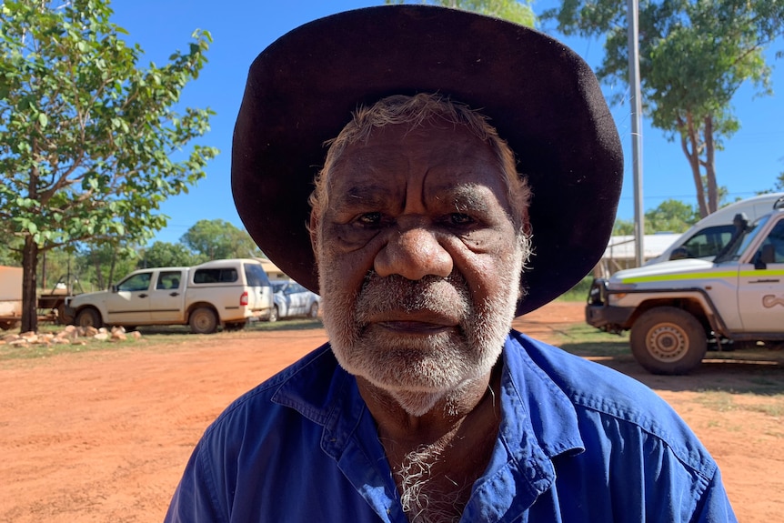 Jack Green in a birght blue work shirt and an Akubra-style hat stands outside with red dirt in the background.