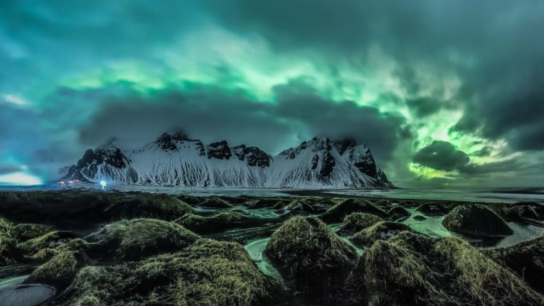 A photo of a snowy island with the cloudy sky lit up with green hues.