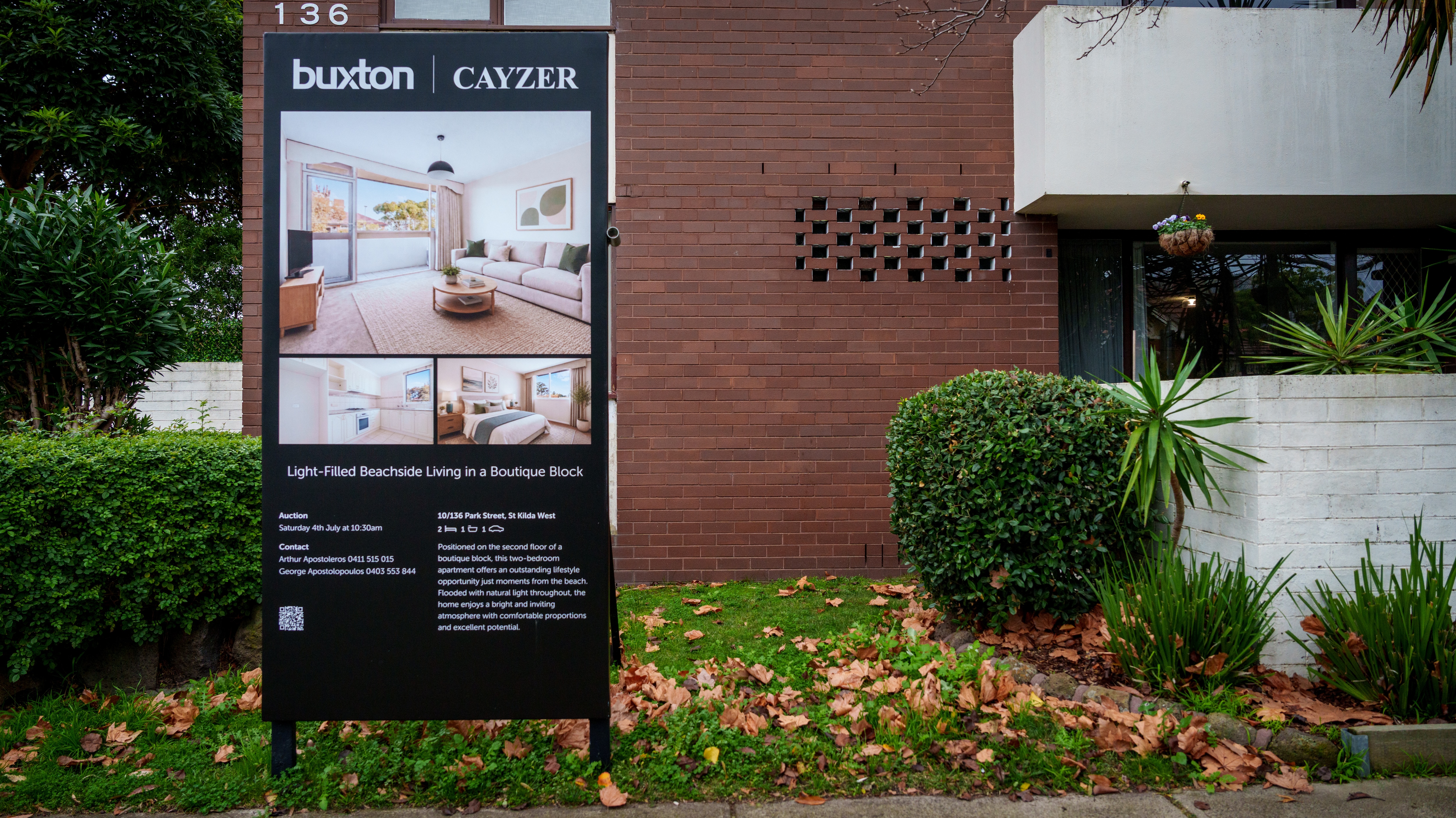 A large sign stands outside a multi-storey brown brick building with real estate information including an auction date.