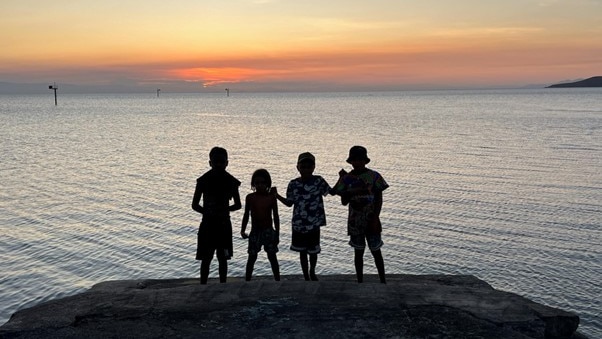 The silhouette of four children standing at dusk on Palm Island, Qld, fading light on the horizon.