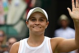 Ashleigh Barty raises her hand and smiles after winning a first-round match at Wimbledon