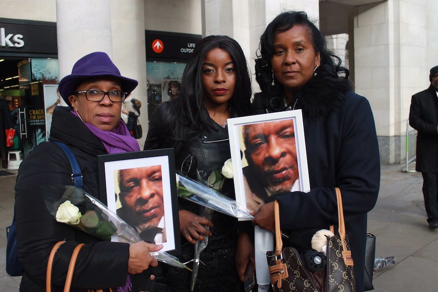 Three women hold up photos of a man killed in the fire.