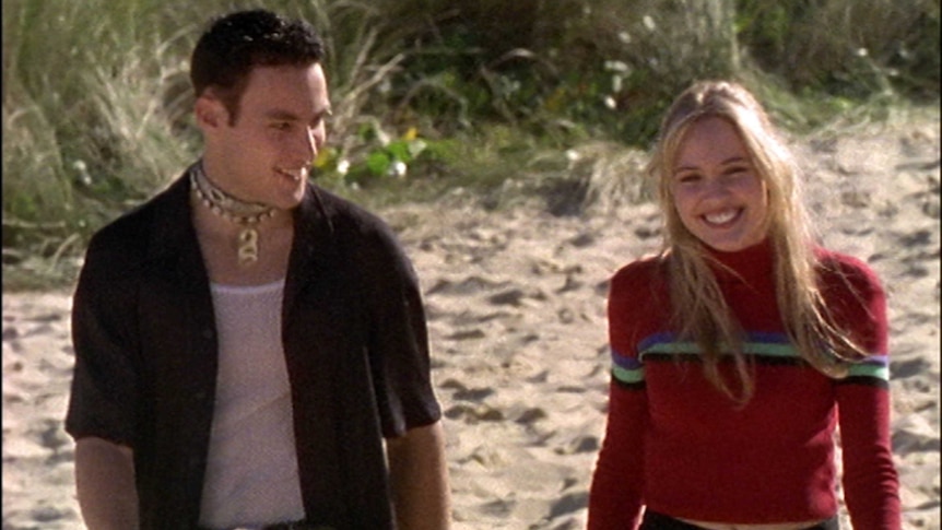 A man and woman walk along a beach laughing