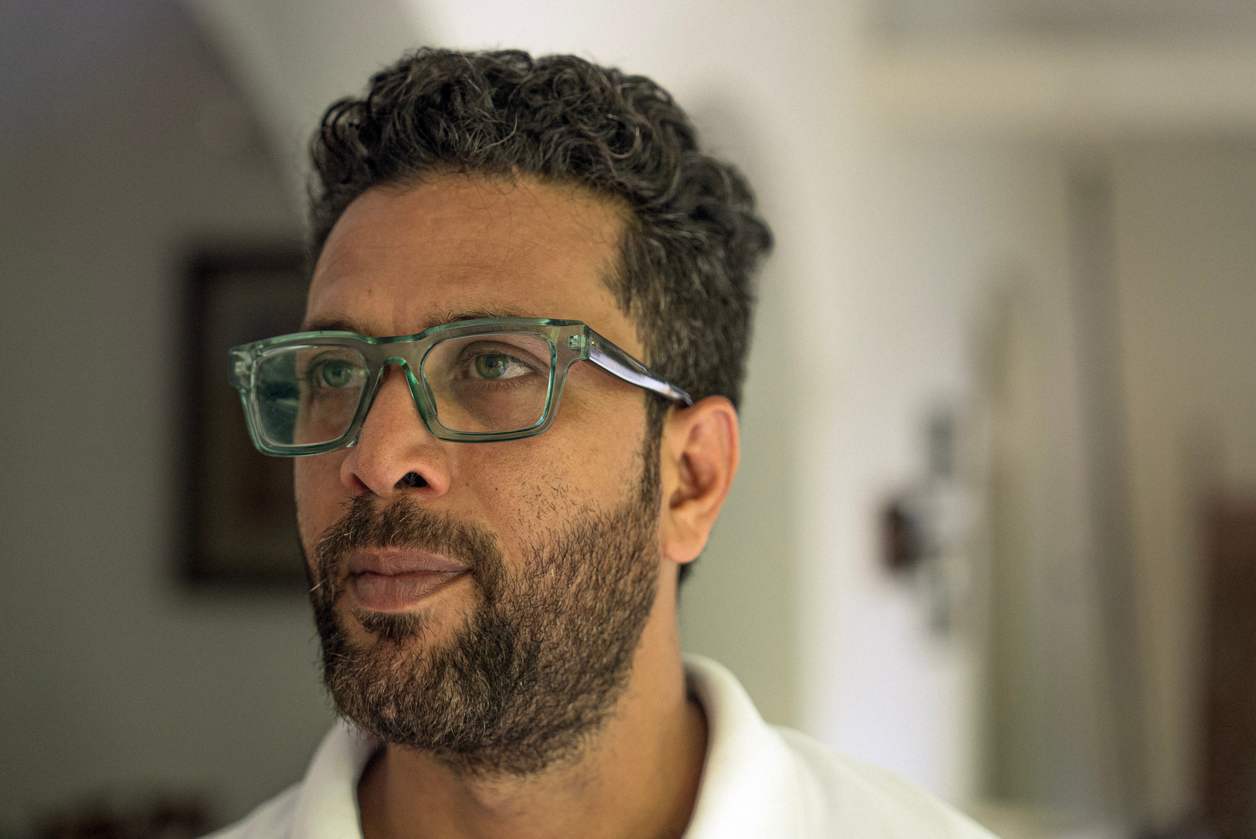 An Indian man with short hair and a beard, wearing glasses with green frames.