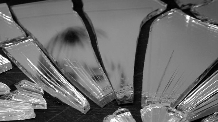 Black and white photo of a smashed mirror with a child's reflection in it.