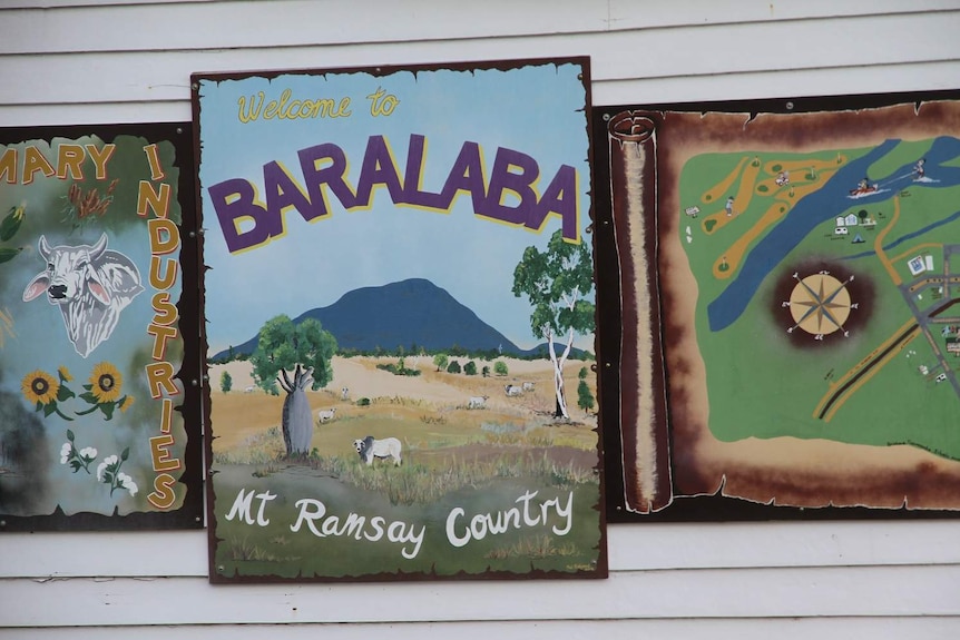 Painted posters on a side of a building, showing a picture of cattle, a picture of a mountain and a picture of a map.