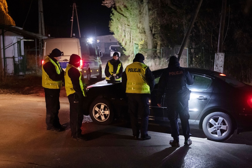 Police officers gather around a car in the night.
