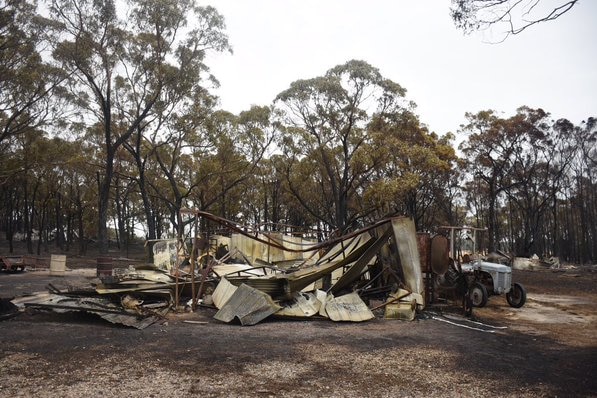 The remains of a burnt house are collapsed beside a burnt tractor.