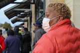 A woman in a red coat and face mask standing in a line outside