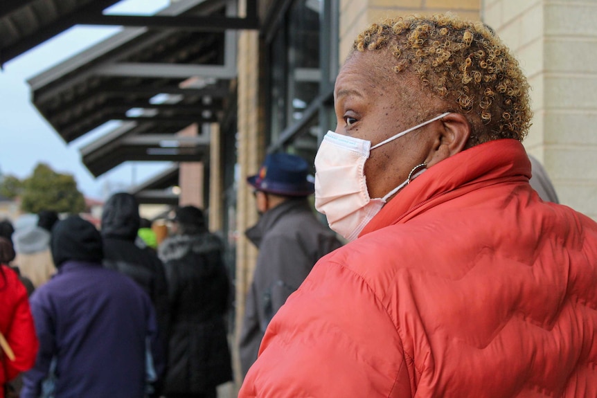 A woman in a red coat and face mask standing in a line outside