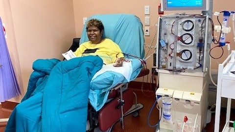 An Aboriginal woman sits at a dialysis chair with a blanket over her. 